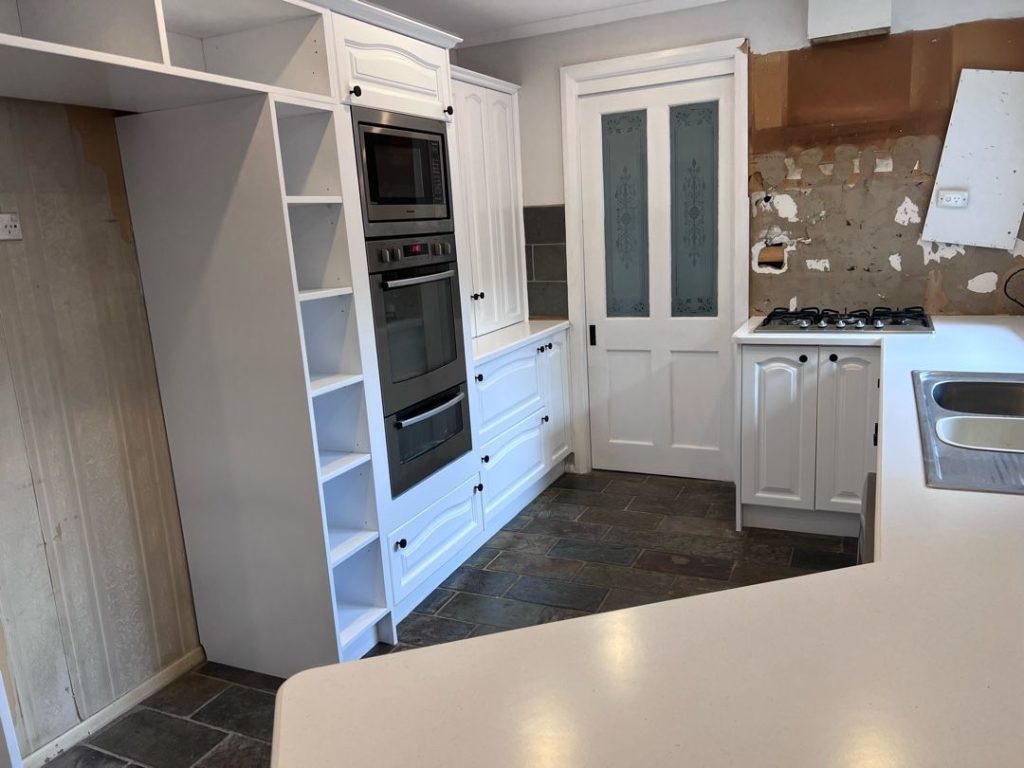 Kitchen under renovation with white cabinets, built-in appliances, and tiled floor.