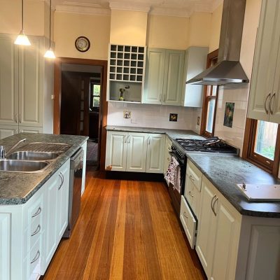 Modern kitchen with wooden floors, light cabinetry, central island, and stainless steel appliances.