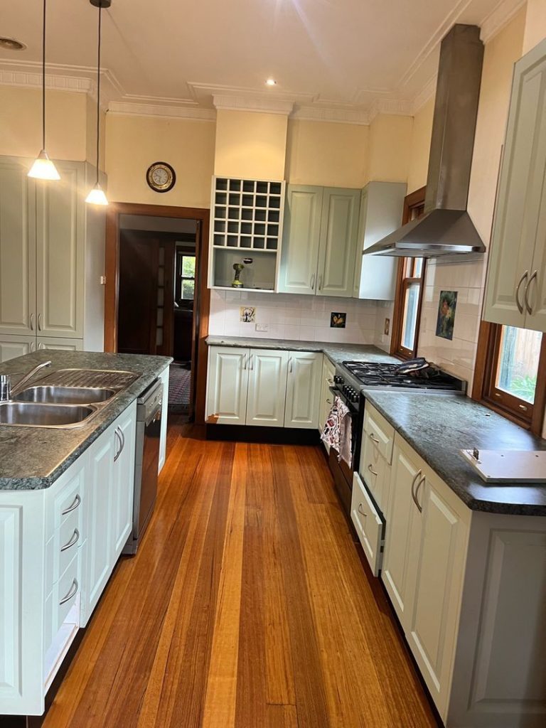 Modern kitchen with wooden floors, light cabinetry, central island, and stainless steel appliances.