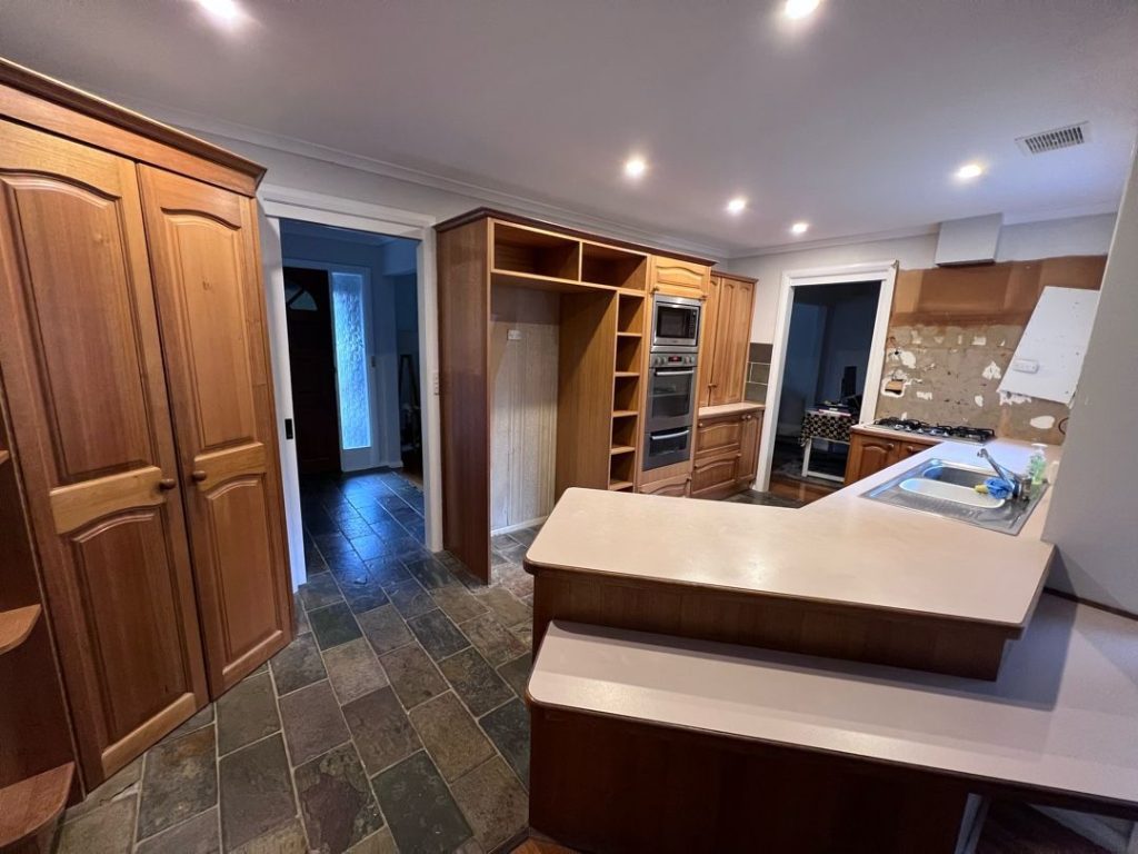 Kitchen with wooden cabinets, built-in appliances, light countertops, double sink, and slate tile flooring.