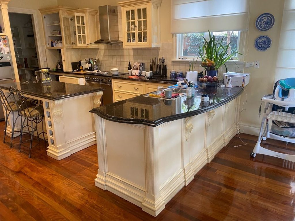 Kitchen with two granite-topped islands, stainless steel appliances, wooden floors, and decorative elements.