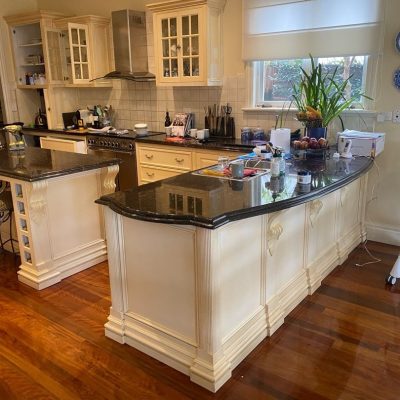 A spacious kitchen with two large islands featuring granite countertops, cream-colored cabinets, stainless steel appliances, and polished hardwood floors.