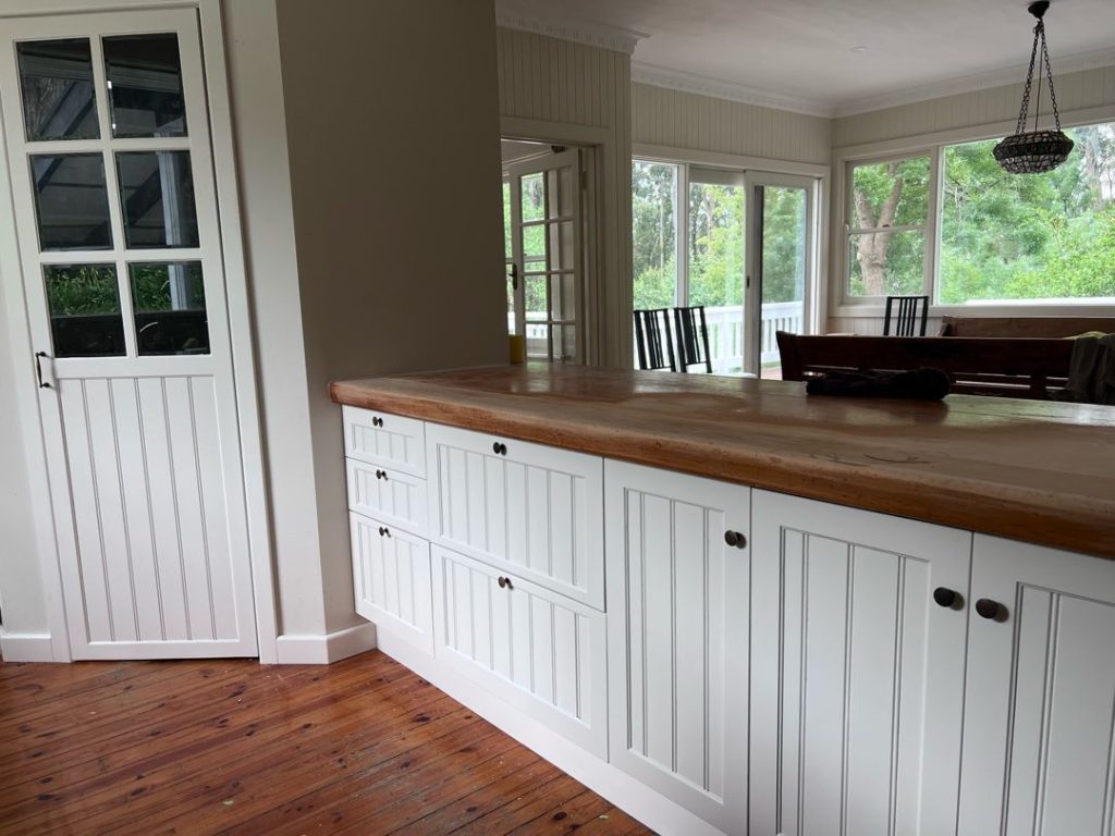 Kitchen with white cabinets and wooden countertop leading to a dining area with large windows.