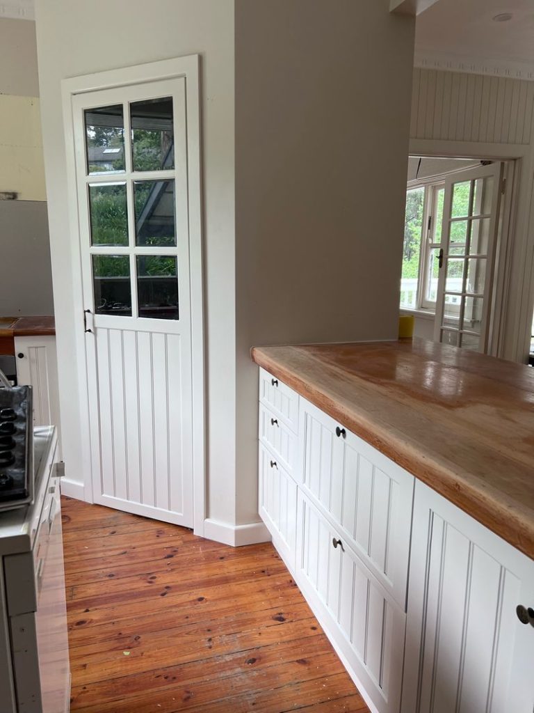 Kitchen area with white cabinets, wooden countertops, a white door with glass panes, and wooden flooring.