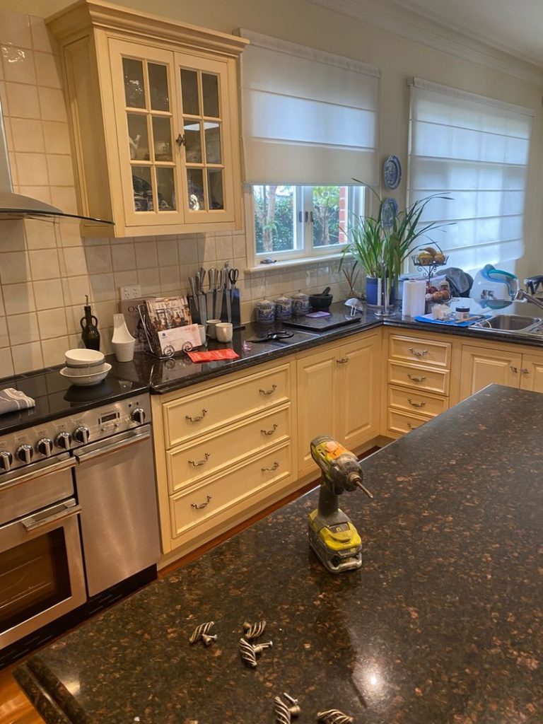 Kitchen interior showing cream cabinets, black granite countertops, stainless steel appliances, and a cordless drill on the island.