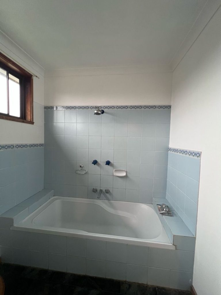 Bathroom with light blue tiles, white bathtub, showerhead, and window.