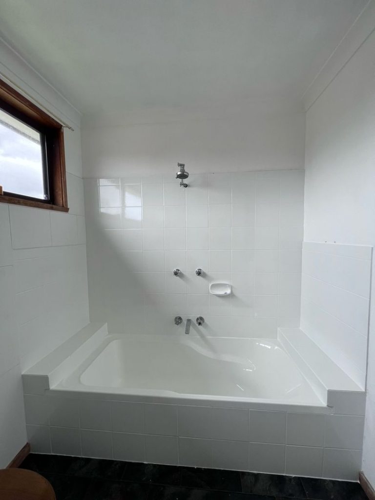 Bathroom with white bathtub, wall-mounted showerhead, and tiled walls