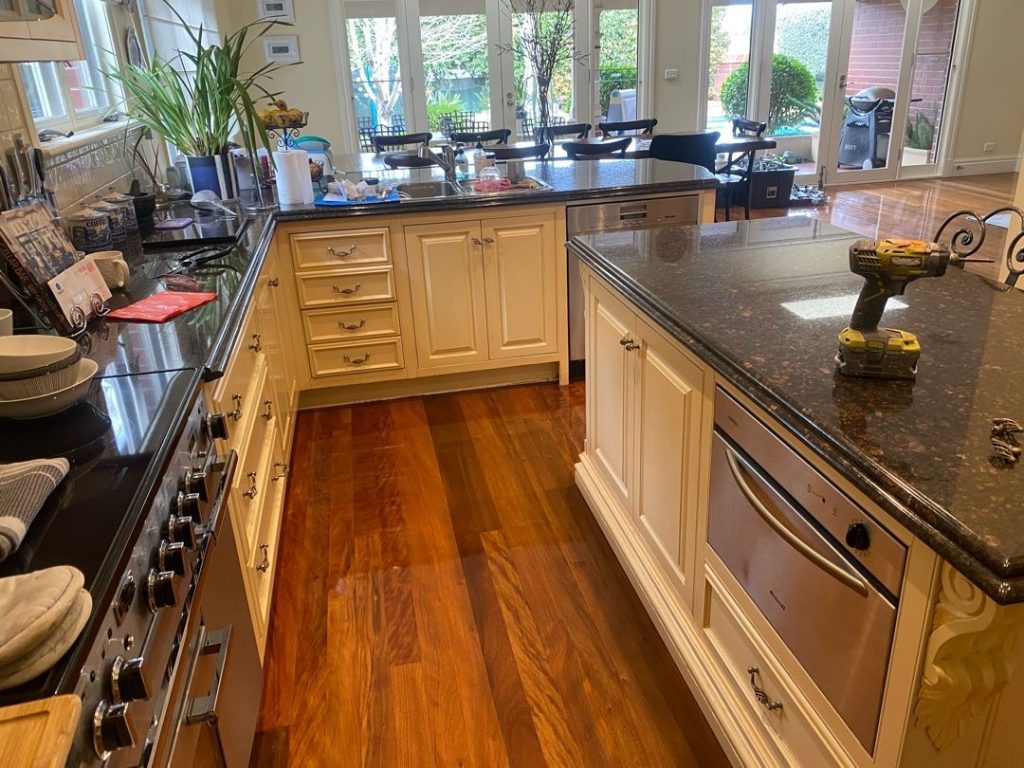 Modern kitchen with granite countertops, white cabinetry, and a drill on the island counter.