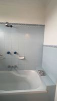 Bathroom with light blue tiles, white bathtub, showerhead, and water control knobs.