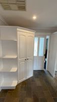 White cabinet with double doors and built-in shelves in a tiled room with a frosted glass door.