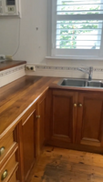 Kitchen with wooden cabinets, wooden countertops, double stainless steel sink, air conditioning unit, and window with white blinds.