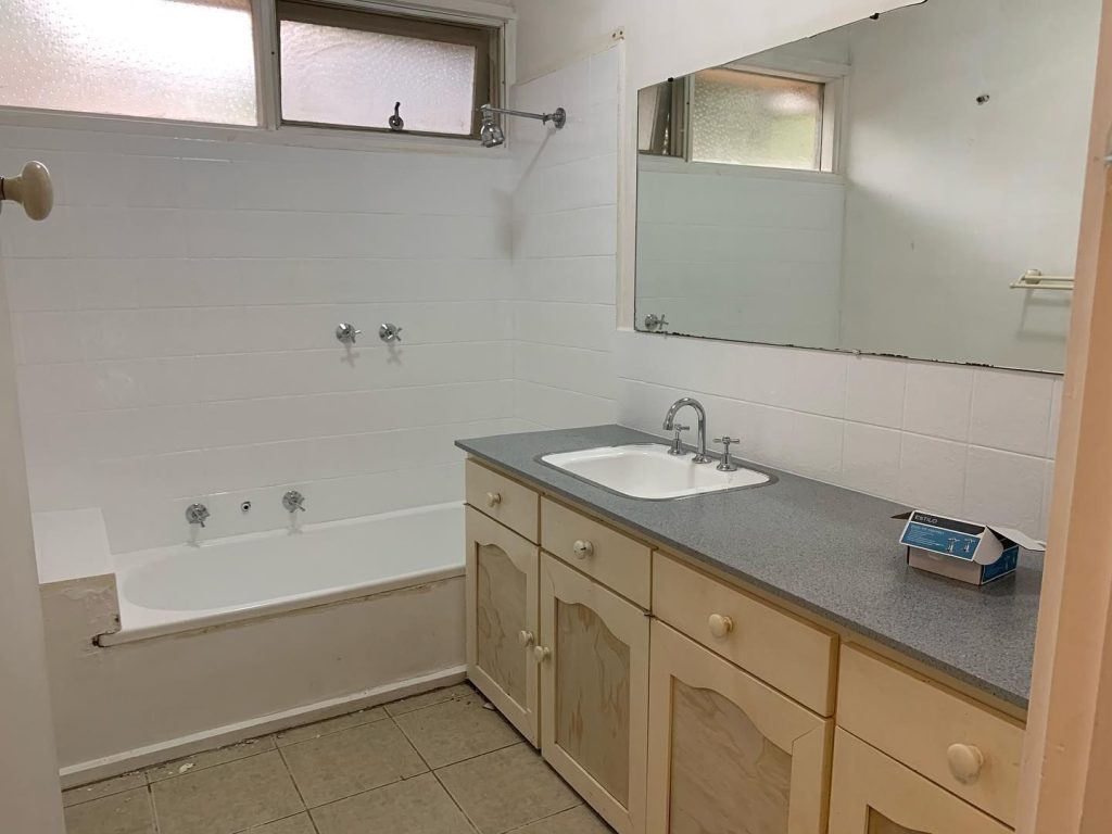 Old bathroom with bathtub, sink, mirror, and worn-out cabinets