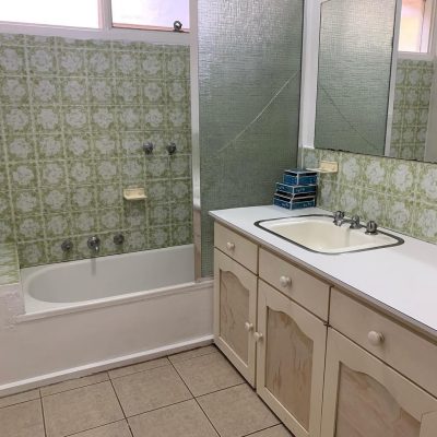 Old bathroom with green tiles, bathtub, and dated vanity