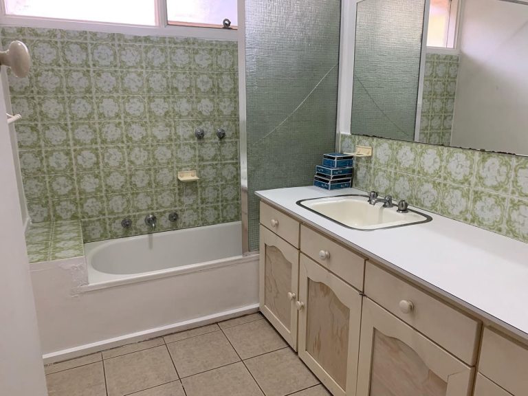 Old bathroom with green tiles, bathtub, and dated vanity