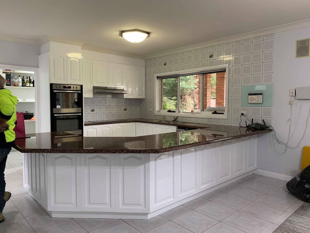 Kitchen with white cabinets, granite countertops, stainless steel appliances, and a person in a neon green jacket.