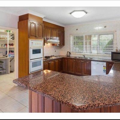 A kitchen with an L-shaped granite countertop, wooden cabinets, double oven, stovetop, range hood, microwave, and visible pantry.