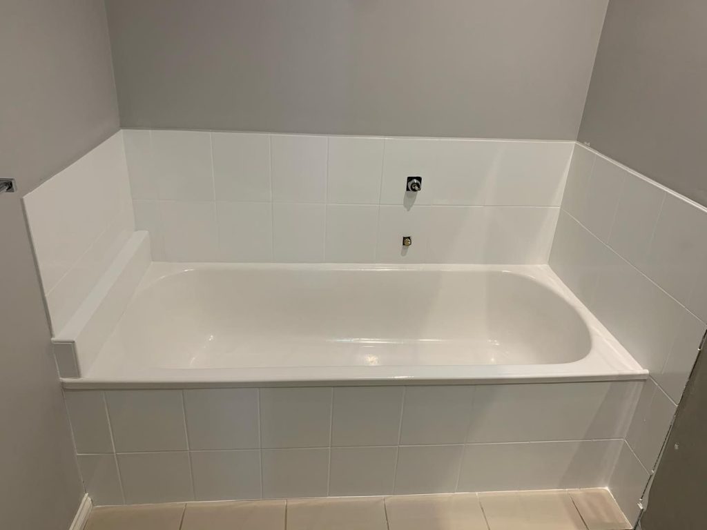 Resurfaced bathroom with new white tiles and a glossy bathtub against gray walls.