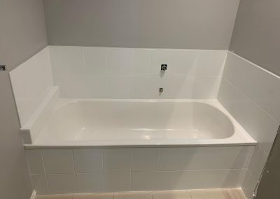 Resurfaced bathroom with new white tiles and a glossy bathtub against gray walls.