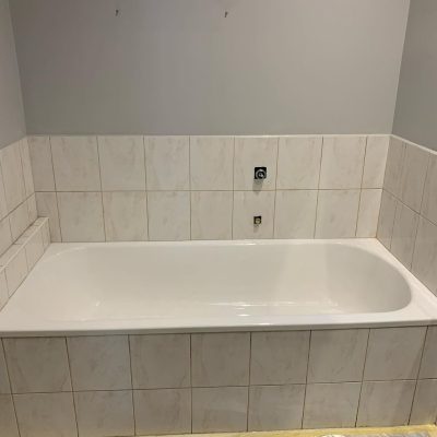 A white bathtub surrounded by new white tiles with a subtle marble pattern in a light gray painted bathroom.