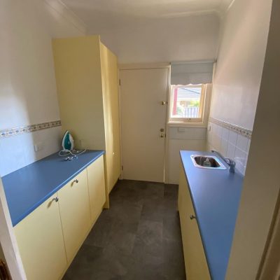 Small utility room featuring yellow cabinets, blue countertops, an iron, and a stainless steel sink.