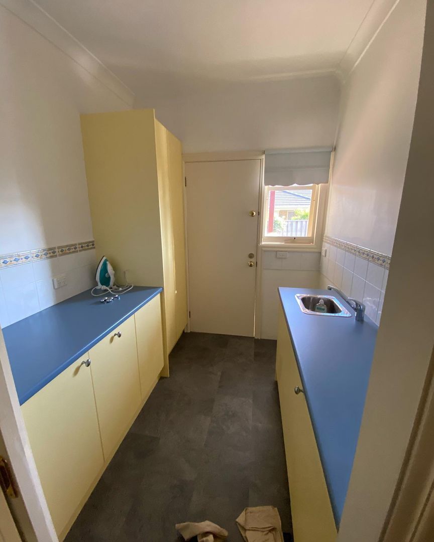 Small utility room featuring yellow cabinets, blue countertops, an iron, and a stainless steel sink.