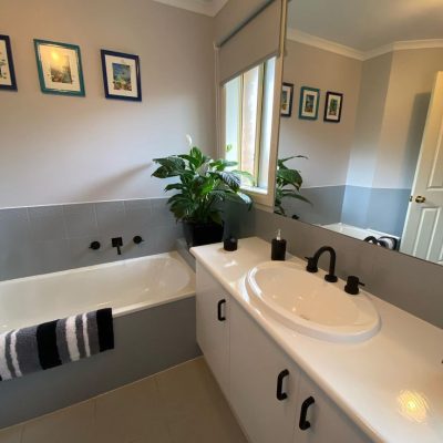 Bathroom featuring a white bathtub, black fixtures, framed pictures, potted plants, and a vanity with black accessories.