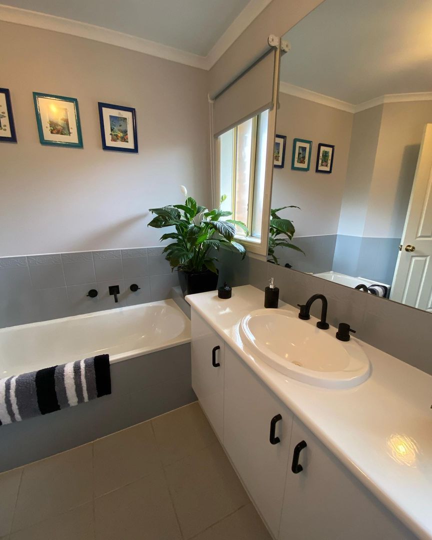 Bathroom featuring a white bathtub, black fixtures, framed pictures, potted plants, and a vanity with black accessories.