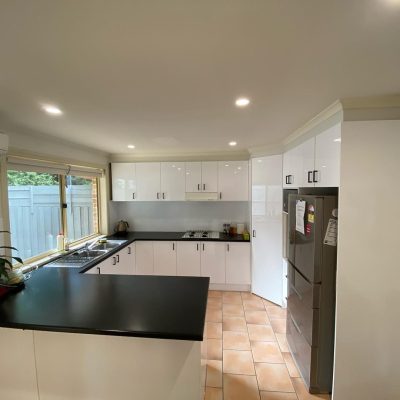 Modern kitchen with white cabinets, black countertops, stainless steel refrigerator, window view of greenery, and recessed lighting.