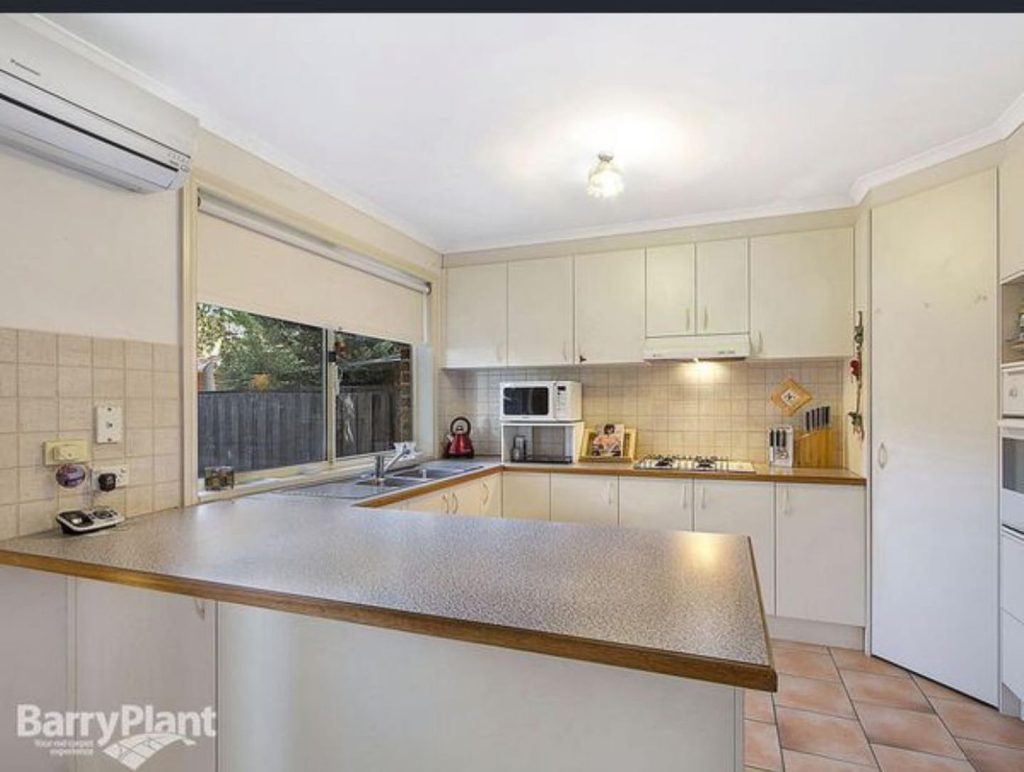 Modern kitchen with beige cabinets, tiled backsplash, and various appliances on the countertop.