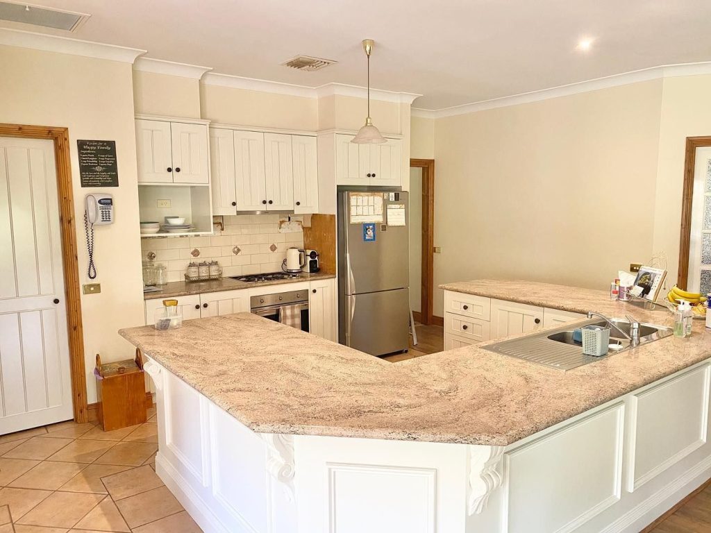 Modern kitchen with white cabinets, granite countertops, stainless steel refrigerator, built-in oven, stovetop, and various kitchen items.