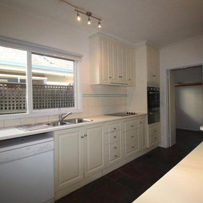 Modern kitchen featuring white cabinets, a benchtop with an integrated sink and dishwasher, a stovetop, and an oven.