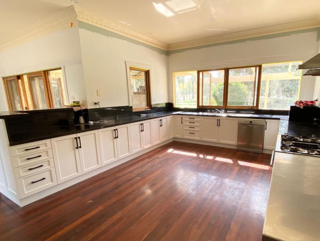 Modern kitchen featuring white cabinets, black countertops, polished dark timber floors, and stainless steel appliances.