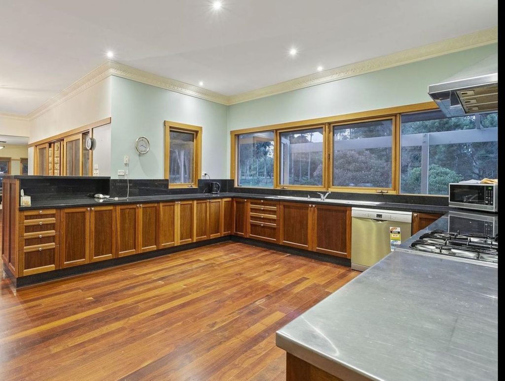 Spacious kitchen with dark wood cabinets, black countertops, stainless steel appliances, and large windows.