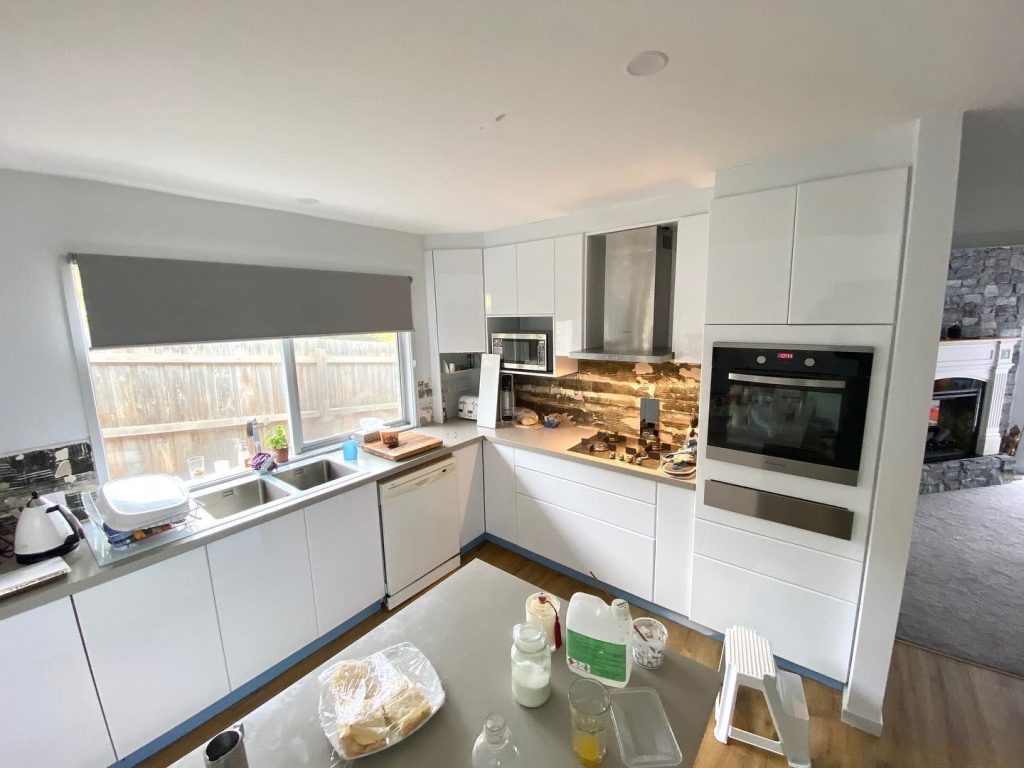 Modern kitchen with white cabinets, stainless steel appliances, double sink, island countertop, and adjoining room with fireplace.