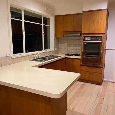 Kitchen with wooden cabinets, tiled backsplash, dual-basin sink, gas stovetop, built-in oven, and unfinished wooden floor.