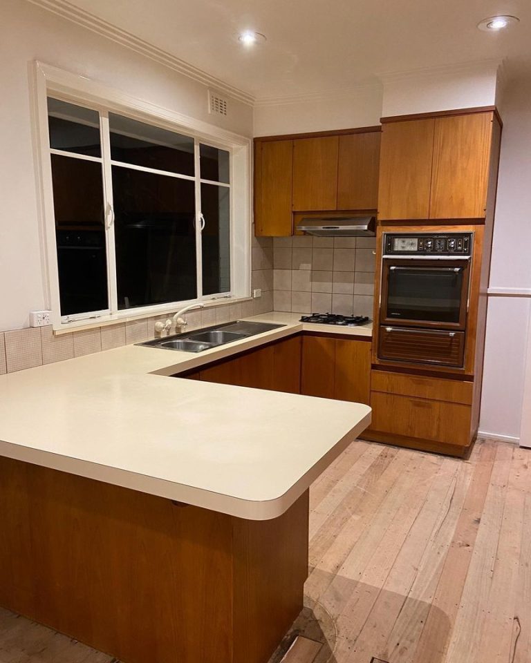 Kitchen with wooden cabinets, tiled backsplash, dual-basin sink, gas stovetop, built-in oven, and unfinished wooden floor.