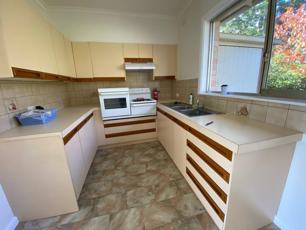 Newly renovated kitchen with beige cabinets, white stove and oven, double sinks, and large window.