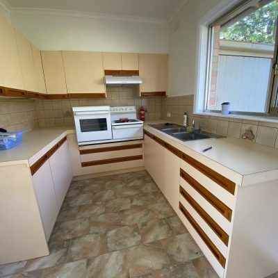 Newly renovated kitchen with beige cabinets, white stove and oven, double sinks, and large window.