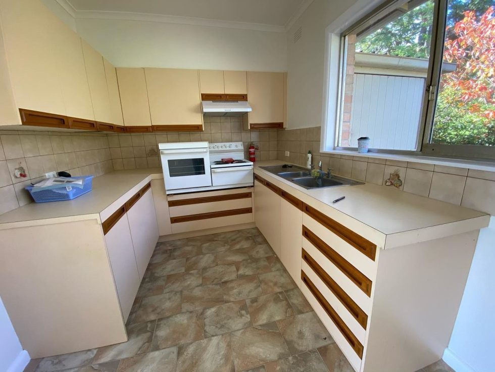 Newly renovated kitchen with beige cabinets, white stove and oven, double sinks, and large window.