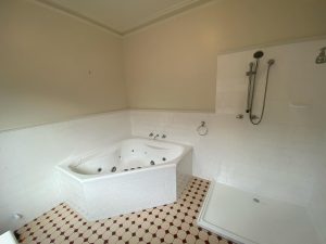 Bathroom with resurfaced white tiles, corner jacuzzi tub, and shower area.