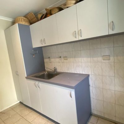 Laundry room with white cabinets, a built-in sink, and various hats stored on top of the cabinets.