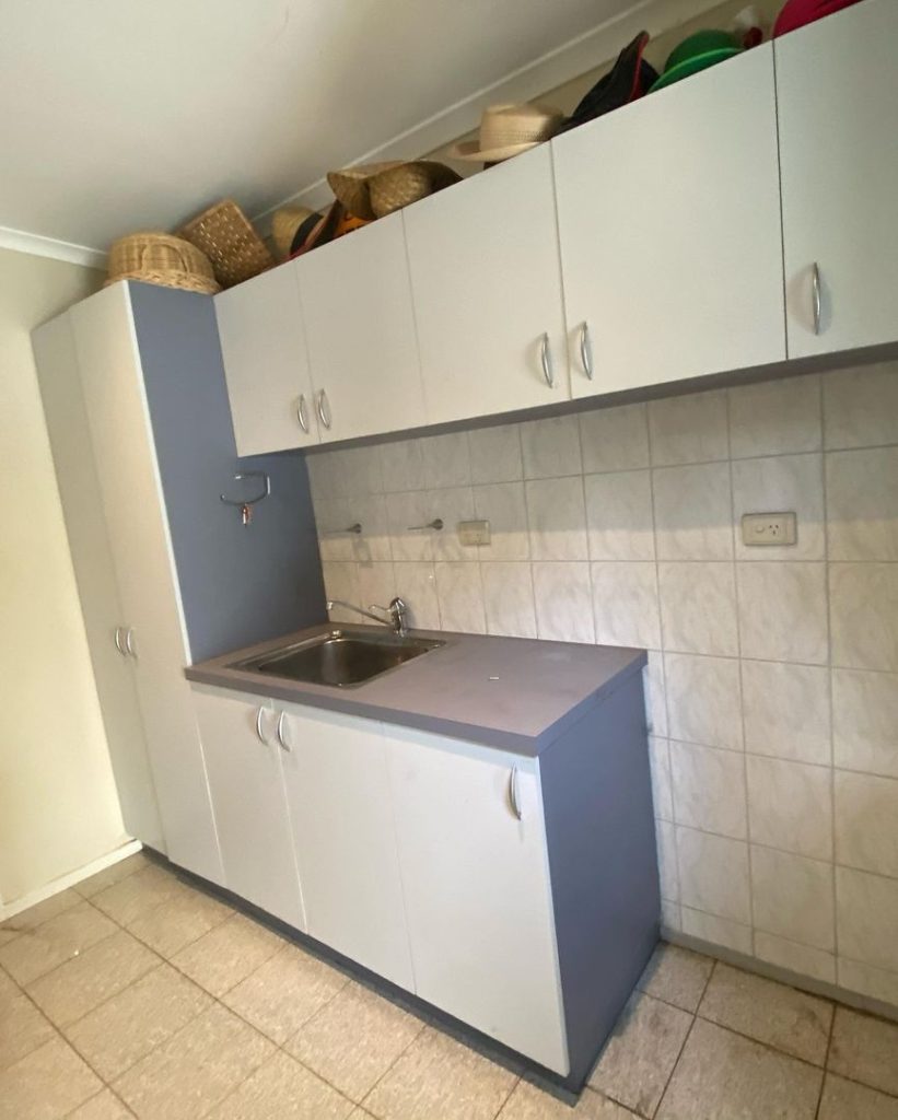 Laundry room with white cabinets, a built-in sink, and various hats stored on top of the cabinets.