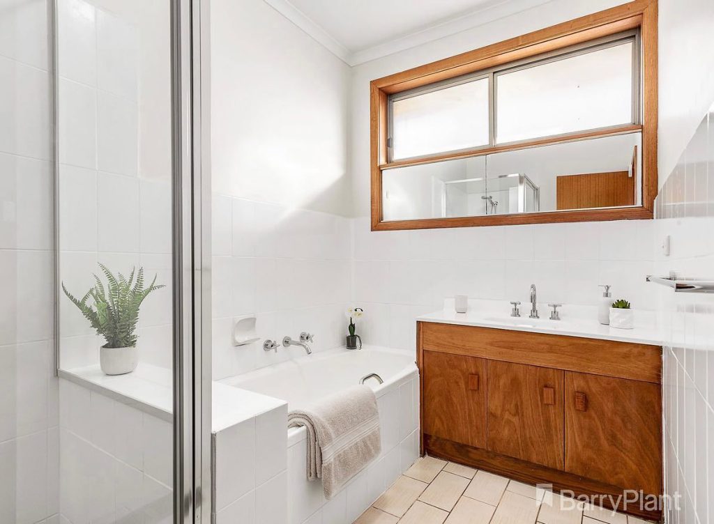 Modern bathroom with white bathtub, wooden vanity, large mirror, and potted plants.