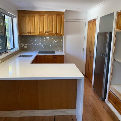 Kitchen with wooden cabinets, white countertops, and partially finished backsplash.