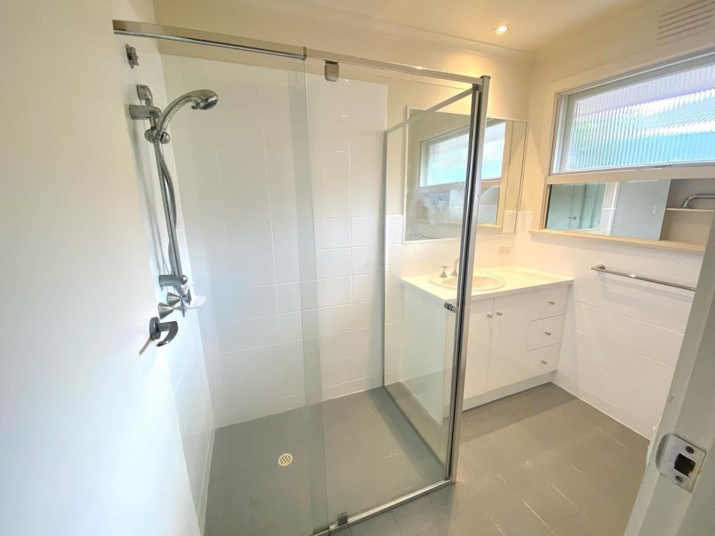 Modern bathroom featuring a glass-enclosed shower, white vanity, and large frosted window.