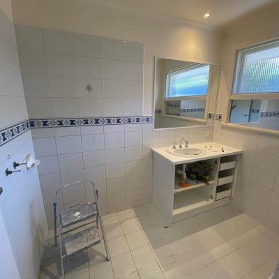 Partially renovated bathroom with white tiles, decorative border, open sink vanity, and step ladder.