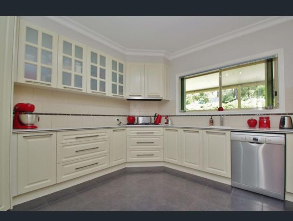 Modern kitchen with cream-colored cabinets and red appliances including a stand mixer, kettle, and toaster.