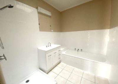 Bathroom with white tiles, bathtub, vanity, showerhead, and light fixture.