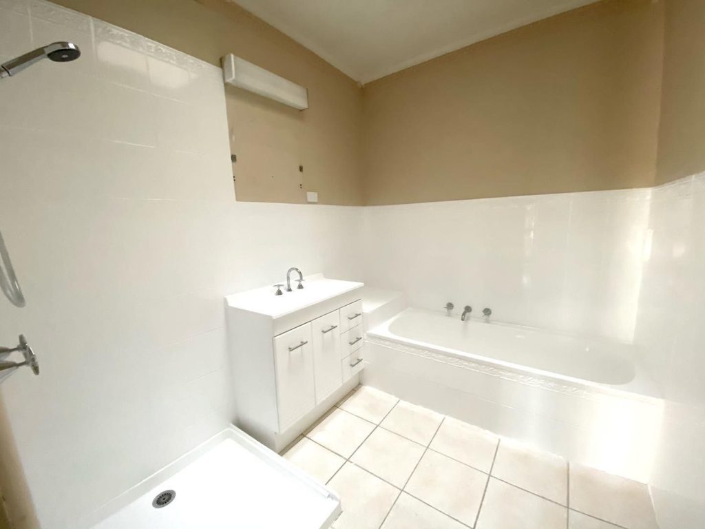 Bathroom with white tiles, bathtub, vanity, showerhead, and light fixture.