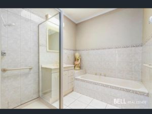 Bathroom with tiled walls, glass shower enclosure, white vanity, and bathtub.